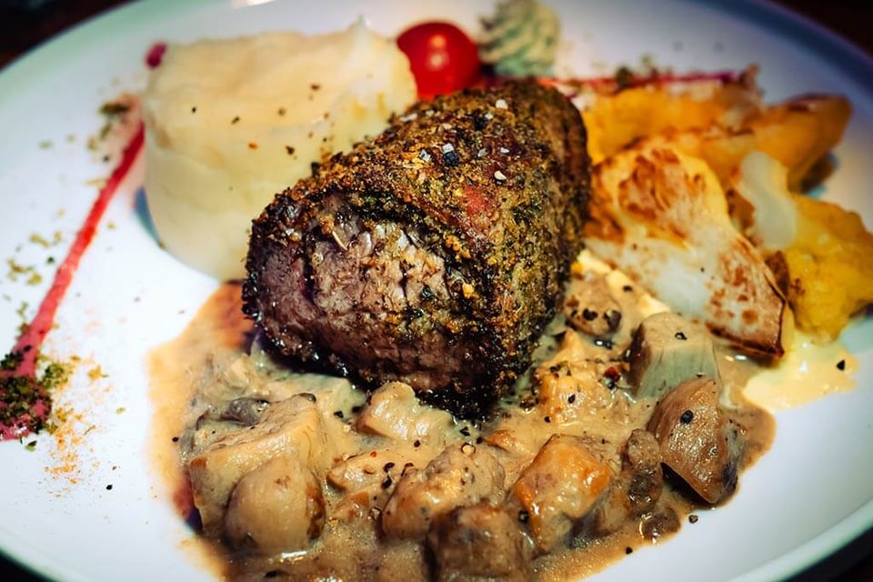 Veal fillet with herb crust, served with creamy porcini mushroom sauce, mashed potatoes, and side dishes.