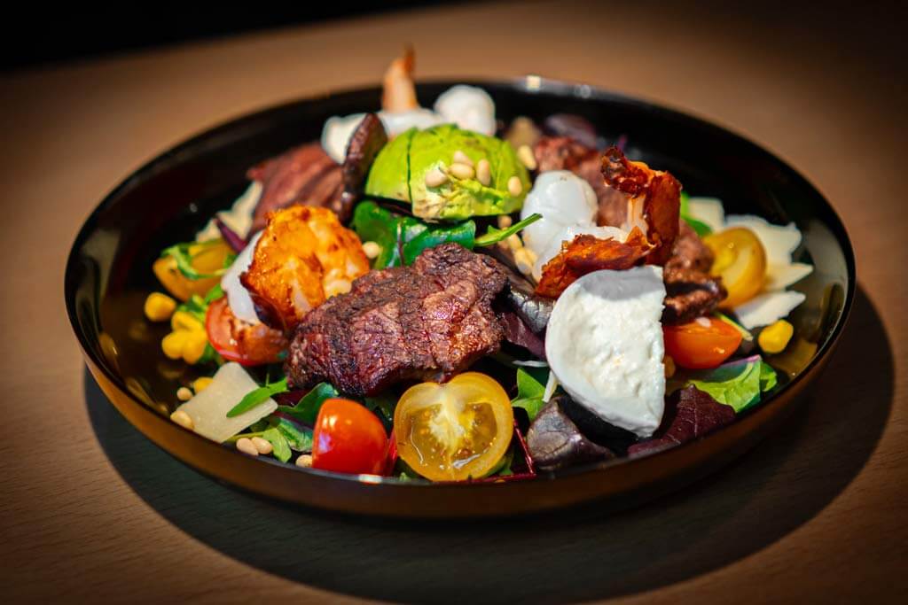 Colorful salad topped with steak pieces, shrimp, avocado, mozzarella, and pine nuts from the Italian restaurant Al Porto in Rostock.