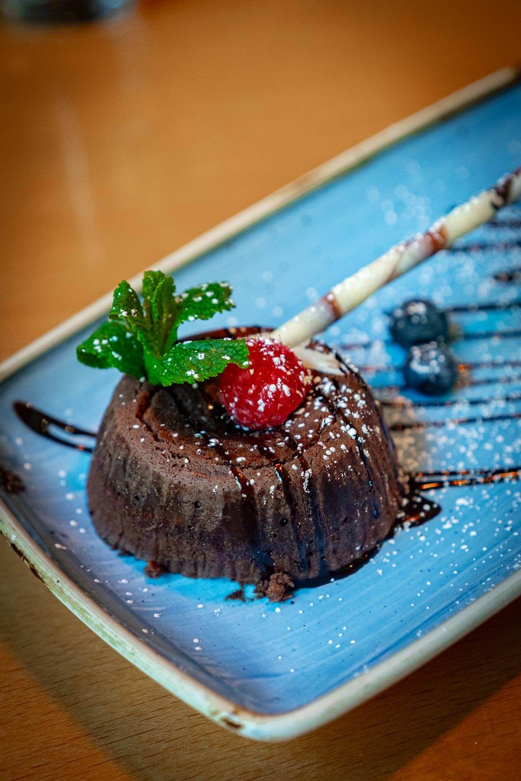 Appetitlicher und frischer Schokoladen-Lava-Kuchen, aus dem Al Porto in Rostock, garniert mit Himbeere, Minze und Waffelröllchen.