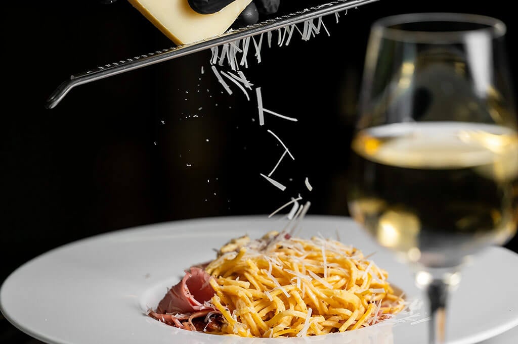 Frisch geriebener Parmesan fällt von einer Reibe auf Pasta vom Italiener Al Porto in Rostock.